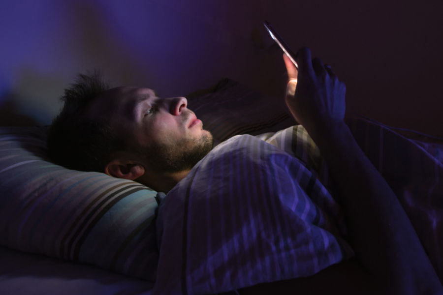 tired man reading on phone before bed